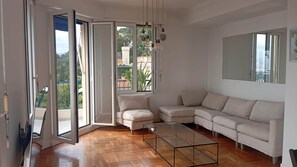 Una sala moderna con una mesa de centro de vidrio, sofá color beige y vistas a un balcón con plantas.