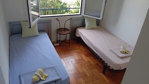 Una habitación pequeña con dos camas individuales, una mesita y una ventana.