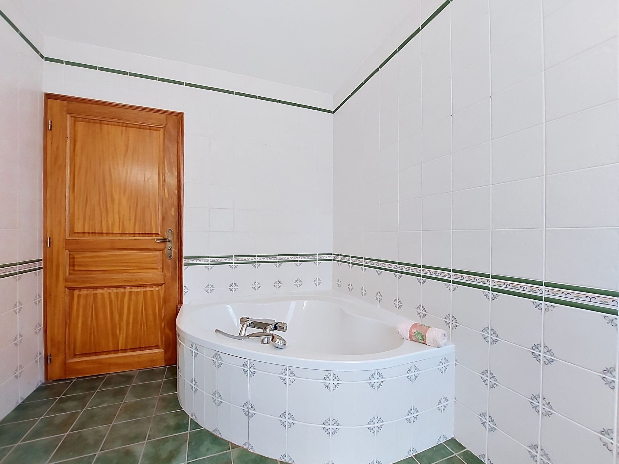 A bathroom with a wooden door, a white bathtub with a faucet, and green-tiled walls.