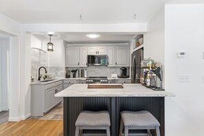 A modern kitchen with grey cabinets, a central island with stools, a built-in oven, and a refrigerator. - Historic Riverside Retreat/Keeney Cove Views (Glastonbury)