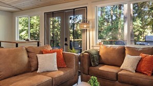 Ein modernes Wohnzimmer mit Ledersofas, einem Couchtisch und großen Fenstern mit Blick auf Bäume.