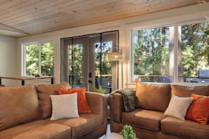 A modern living room with leather sofas, a coffee table, and large windows with a view of trees.