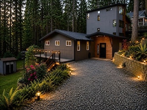 Una casa moderna de dos pisos con entrada de grava, rodeada por un bosque.