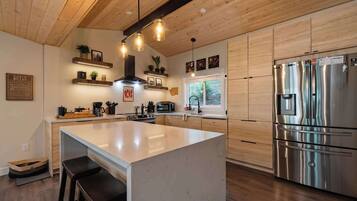 A modern kitchen with wooden cabinetry, a stainless steel refrigerator, and a central island with bar stools.