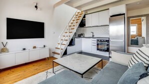 Ein modernes Wohnzimmer mit Flachbildfernseher, Sofa, Couchtisch und einer Treppe, die zur Küche hinaufführt.