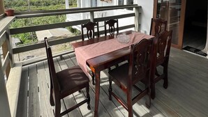 Een houten terras met een tafel en stoelen, met uitzicht op een huis en groen.