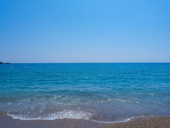 Une plage à l’eau d’un bleu limpide et au rivage de galets.