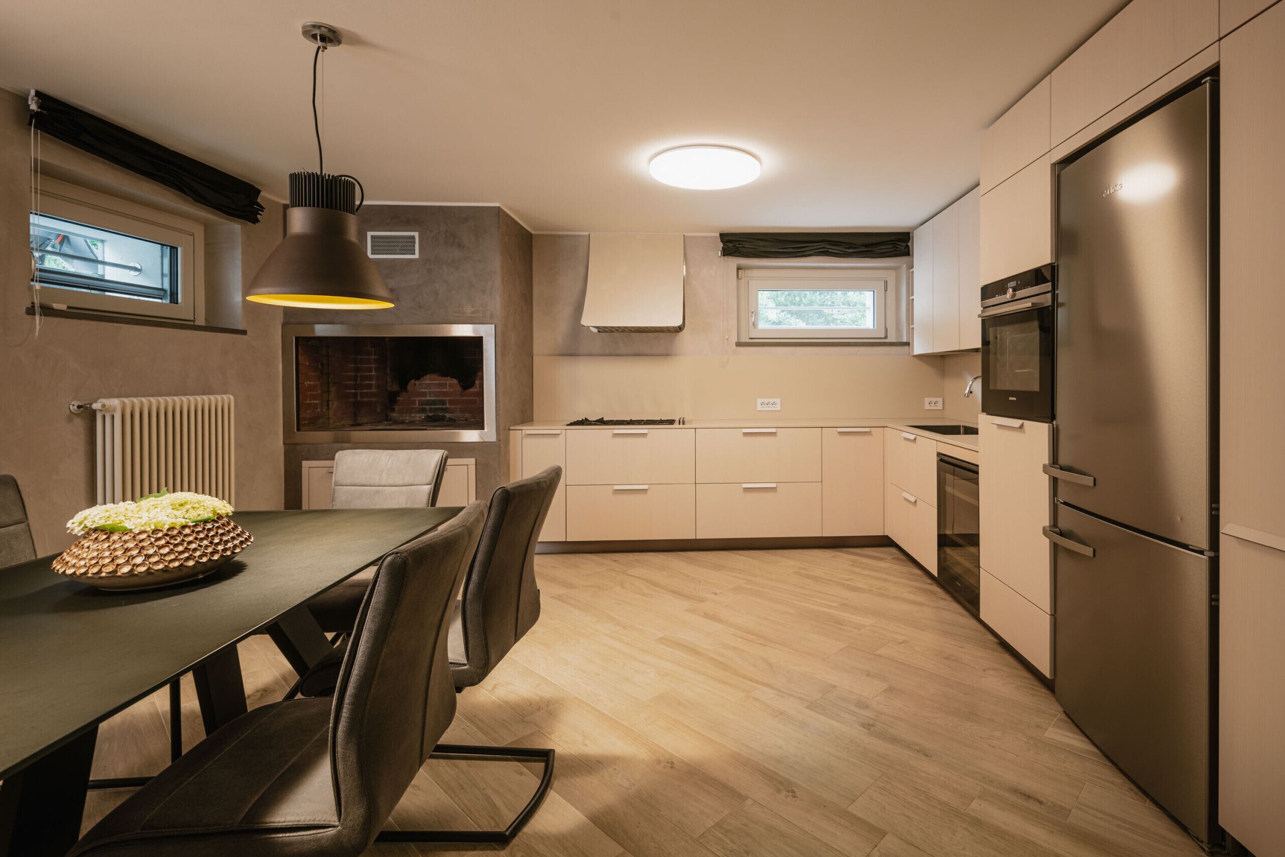 A modern kitchen with a dining table, chairs, a hanging light fixture, and built-in appliances.