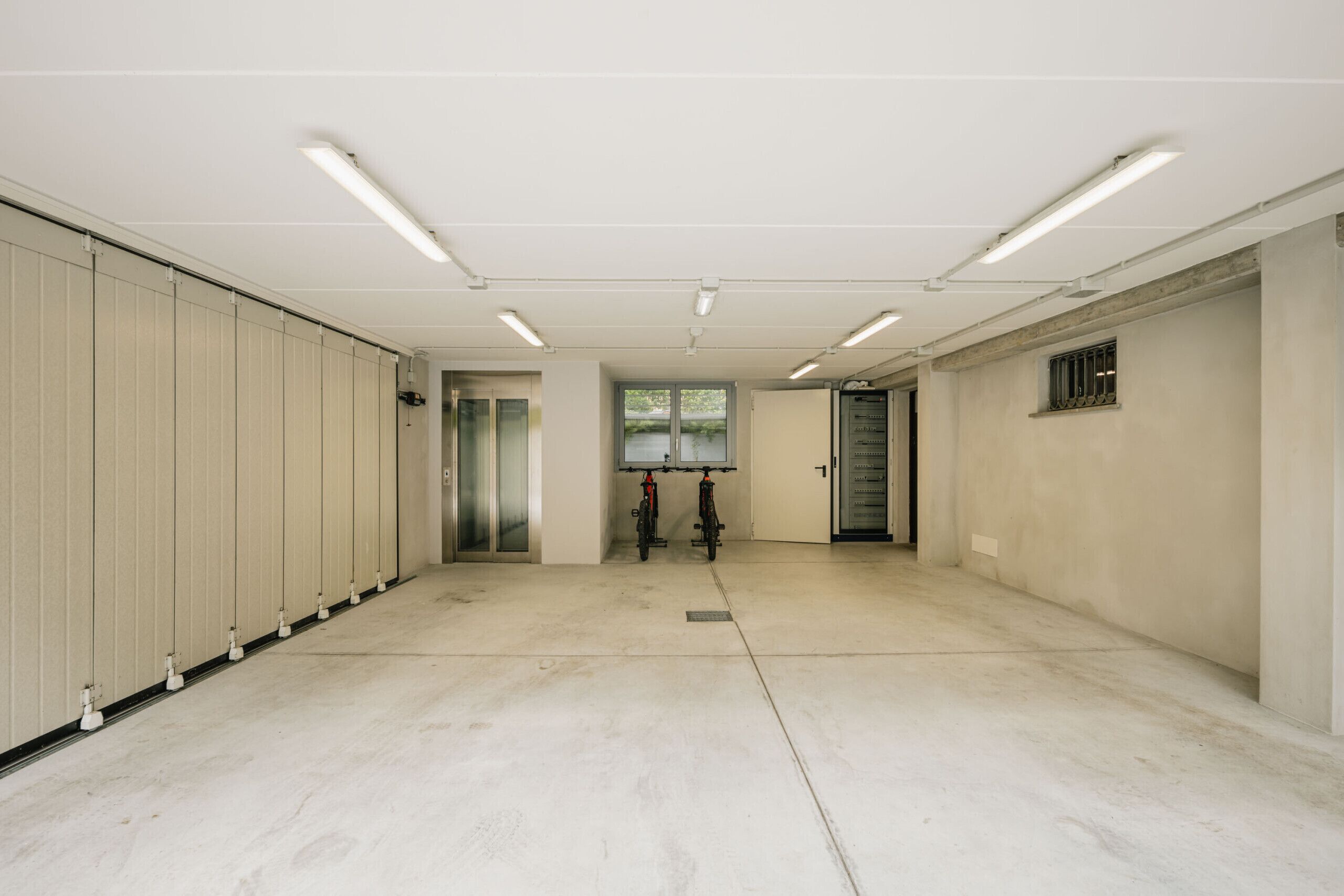 A spacious, well-lit hallway with lockers, a door leading to another room, and two bicycles parked near the door.