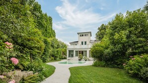 Una casa moderna con piscina, rodeada de abundante vegetación y un césped cuidado.