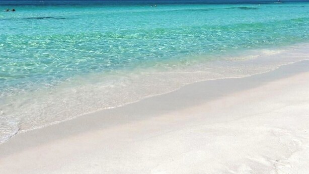 Ein Strand mit klarem türkisblauem Wasser und weißem Sand.