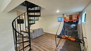 A room with a spiral staircase, a grey sofa, a basketball hoop, and a basketball net. - 3-Bedroom private lake cabin with access to state park and boat ramp (Pittsburg)