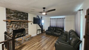 A living room with a stone fireplace, a leather sofa, a ceiling fan, and a television mounted on the wall. - 3-Bedroom private lake cabin with access to state park and boat ramp (Pittsburg)