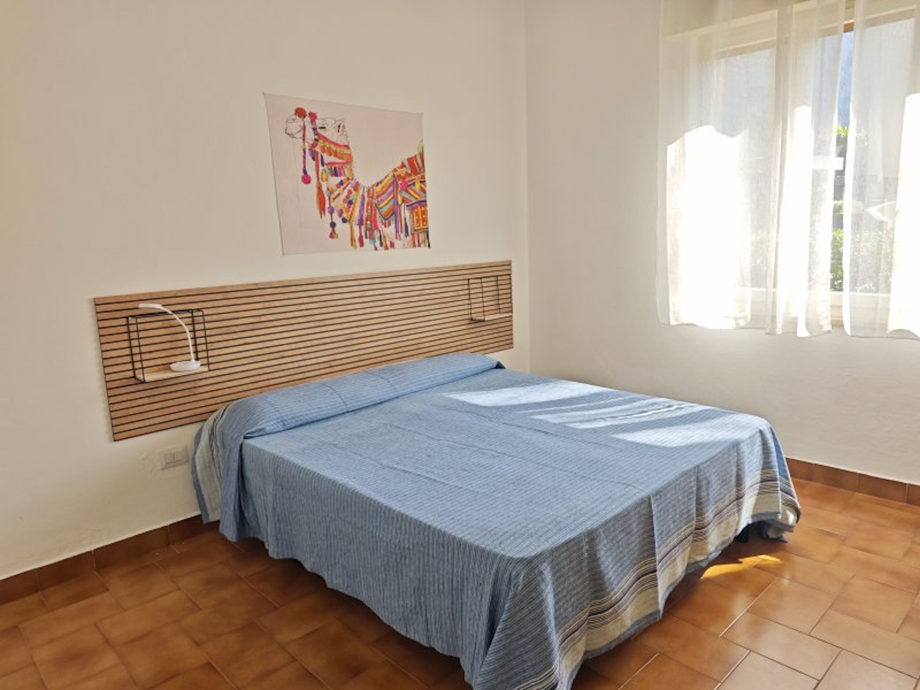 Een slaapkamer met een bed, hoofdeinde, een wandlamp en een raam met gordijnen.
