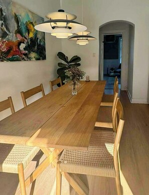 Ein Esszimmer mit Holztisch, sechs Stühlen, einer Blumenvase und einem Bild an der Wand.