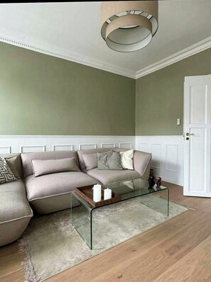 Ein Wohnzimmer mit einem Ecksofa, einem Glastisch und einer modernen Deckenleuchte.