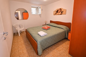 Ein Schlafzimmer mit einem Bett, einem Sessel, einem Fenster, einem Wandspiegel und einer Tür.