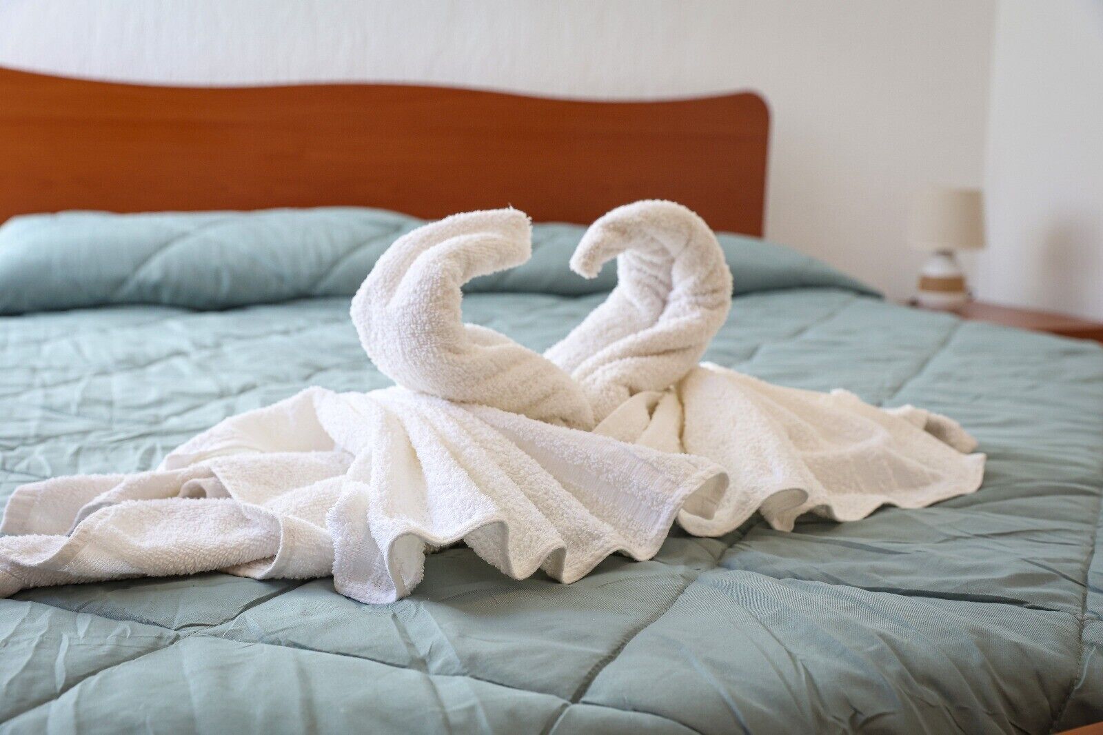 Un lit avec une couette verte et une serviette blanche disposée en forme de cygne.
