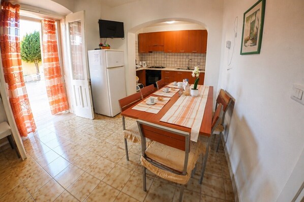 A kitchen with a dining table, chairs, a refrigerator, and a TV mounted above the counter.