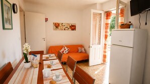 A compact room with a dining table set for two, a sofa, a refrigerator, and a door leading to a balcony.