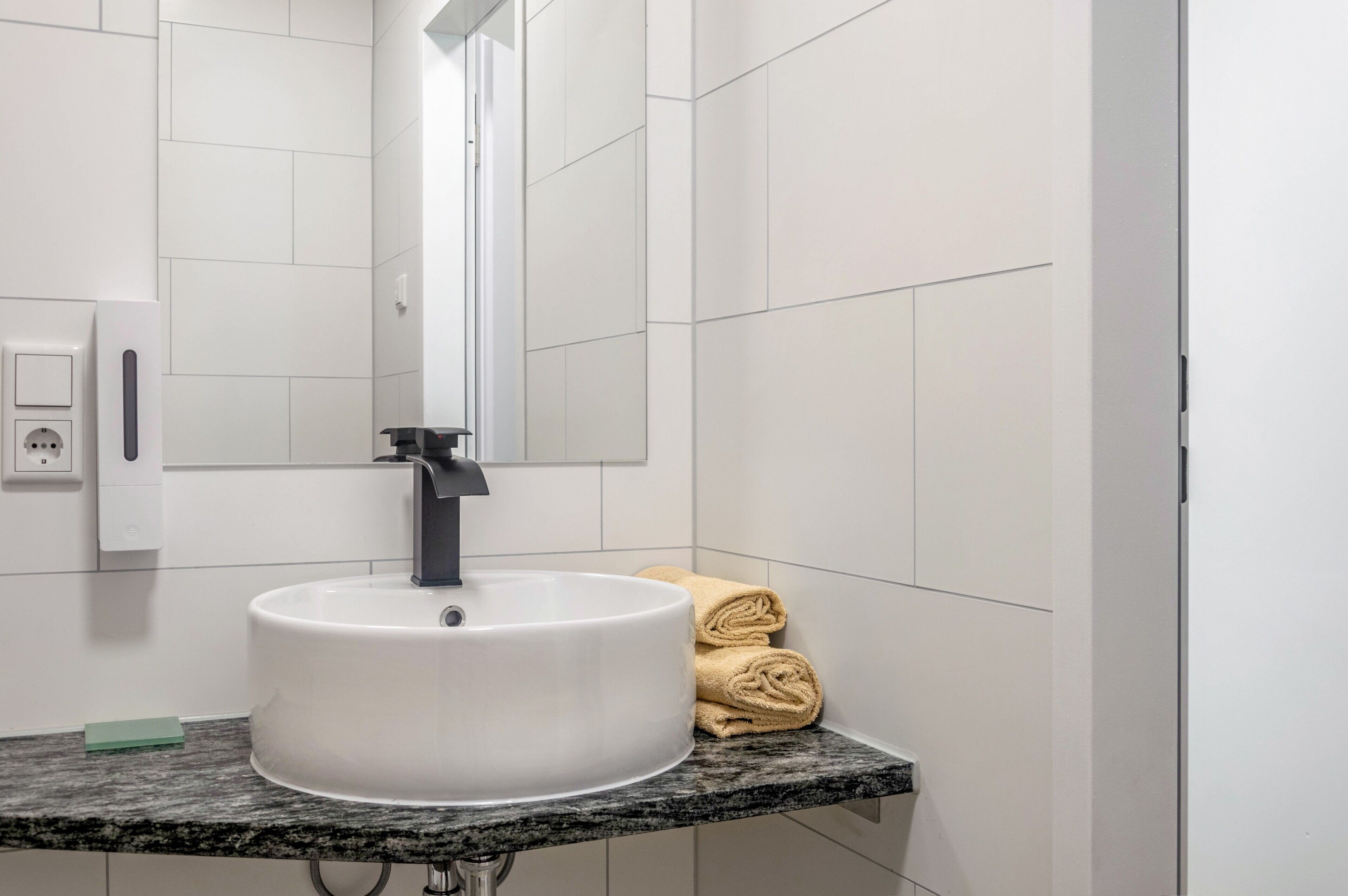 Une salle de bain avec un lavabo blanc, un miroir, un porte-serviettes et un distributeur de savon.