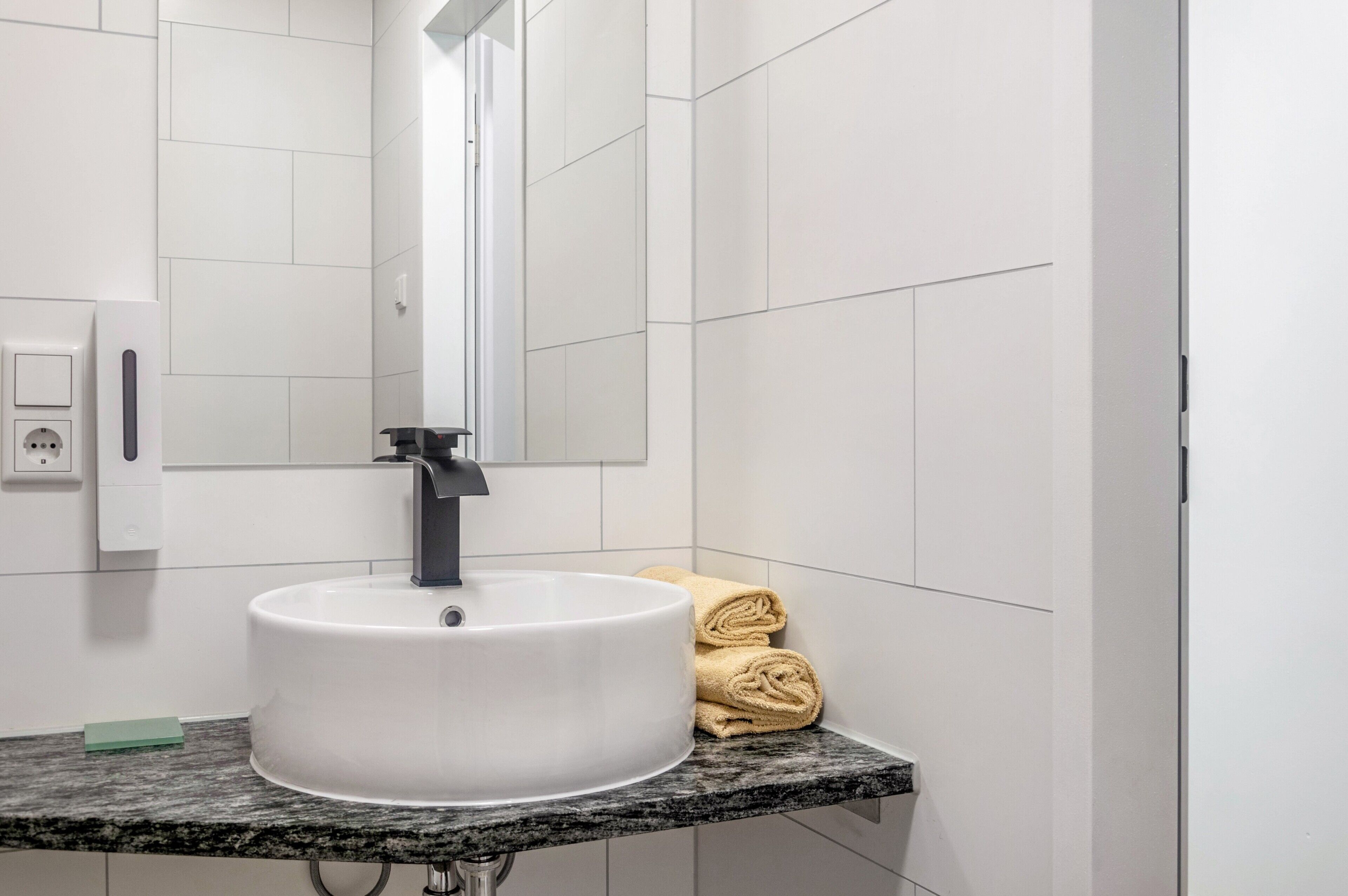A bathroom with a white sink, a mirror, a towel rack, and a soap dispenser.