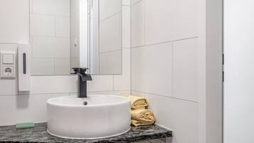A bathroom with a white sink, a mirror, a towel rack, and a soap dispenser.