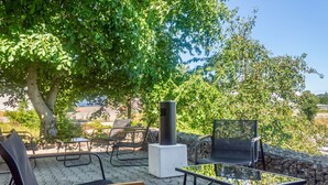 Un espace extérieur aménagé avec une table et des chaises, un foyer et une vue sur des arbres et un bâtiment en arrière-plan.