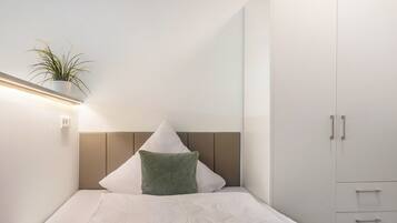 Quarto minimalista com uma cama, um travesseiro verde, um travesseiro branco, uma planta na mesa de cabeceira e um guarda-roupa.