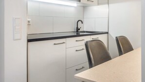 Une cuisine moderne avec des meubles blancs, un plan de travail noir et un robinet en acier inoxydable. Il y a deux chaises autour d’une table.