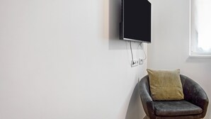 Un soggiorno moderno con una TV a schermo piatto montata, una poltrona con un cuscino e una finestra che lascia entrare luce naturale.