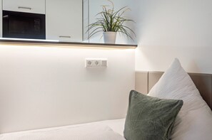 A bedroom with a bed, a pillow, a bedside table, a wall socket, and a potted plant. - Studio Apartment '4' with Wi-Fi (Parsberg)