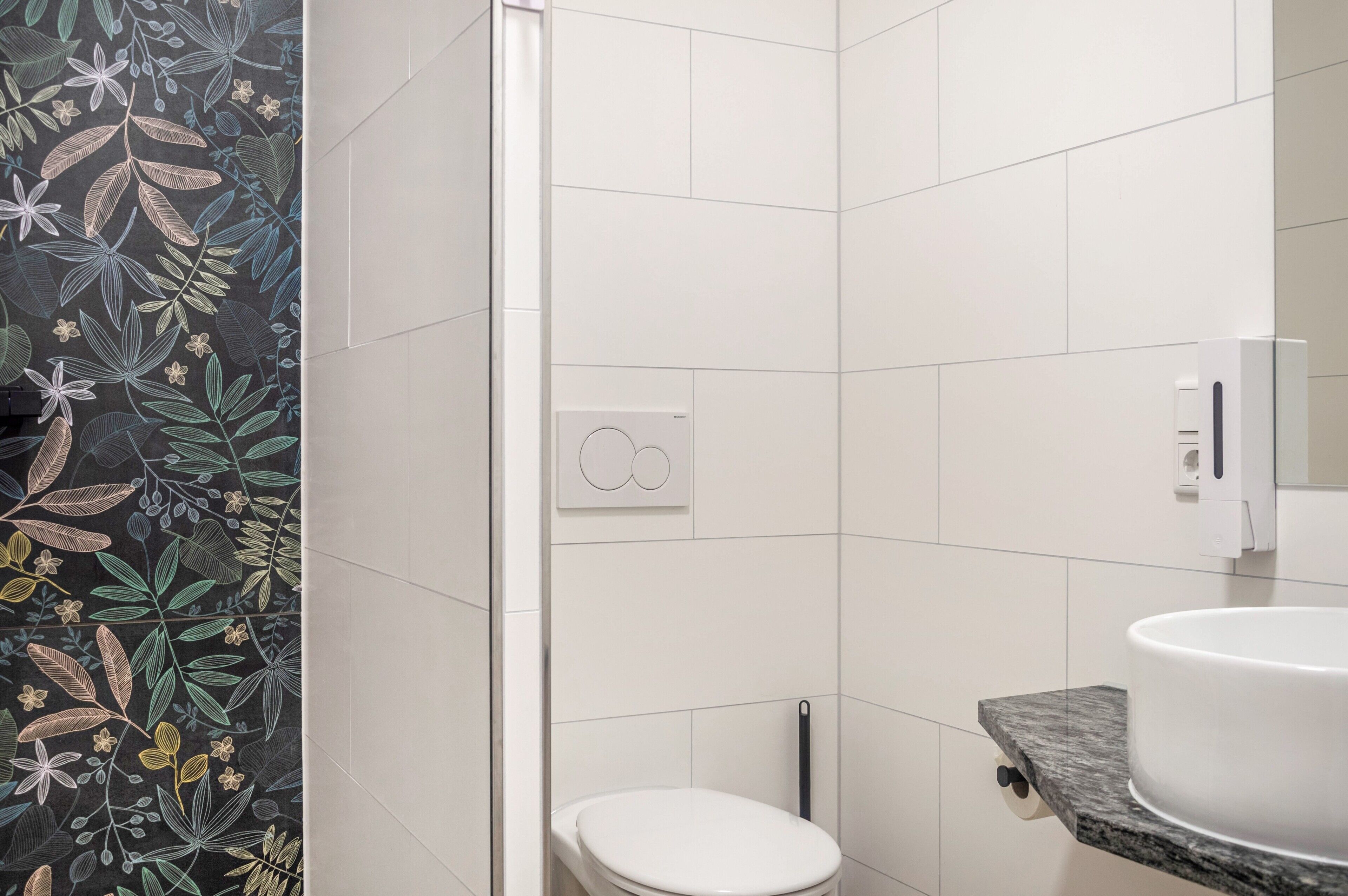 Een badkamer met witte tegels, een toilet, een wastafel met een marmeren blad en een douchehoek.