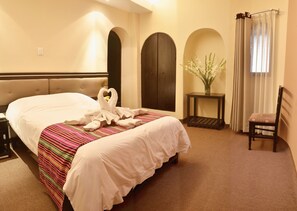 Una habitación de hotel con una cama, una silla, una mesita y un florero con flores.