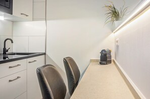 Una cucina con lavello, pensili, due sedie, una pianta e una macchina per il caffè.