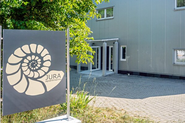 A sign for JURA apartments with a modern building in the background.