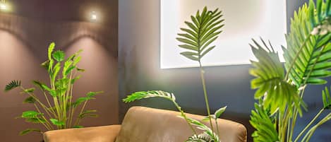 Un salón moderno con un sofá, plantas grandes en macetas y una pantalla de proyector montada en la pared.