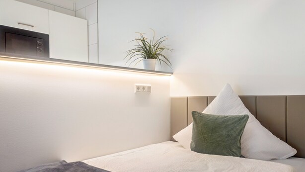 A hotel room with a bed, a bedside table, a lamp, a plant, and a wall-mounted cabinet. - Studio Apartment '8' with Wi-Fi (Parsberg)