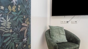 A room with a flat-screen TV mounted on the wall, a green armchair with a cushion, and a decorative wall with a leaf pattern. - Studio Apartment '8' with Wi-Fi (Parsberg)