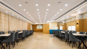 A conference room with multiple tables and chairs, a wooden accent wall, and a large window. - Deluxe JR Royals (Golmuri)