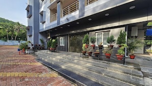 Un edificio moderno con entrada pavimentada, plantas en macetas y una vista despejada del entorno verde.