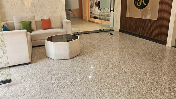 Un vestíbulo con piso de mármol, un sofá con cojines, un separador de vidrio y una pared con un logotipo.