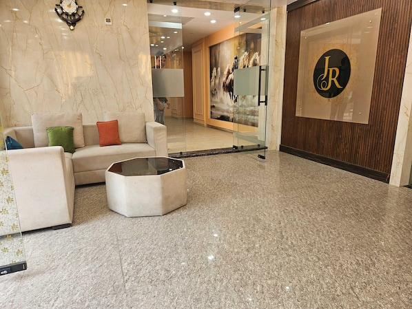 A lobby with a marble floor, a sofa with cushions, a glass partition, and a wall-mounted clock.
