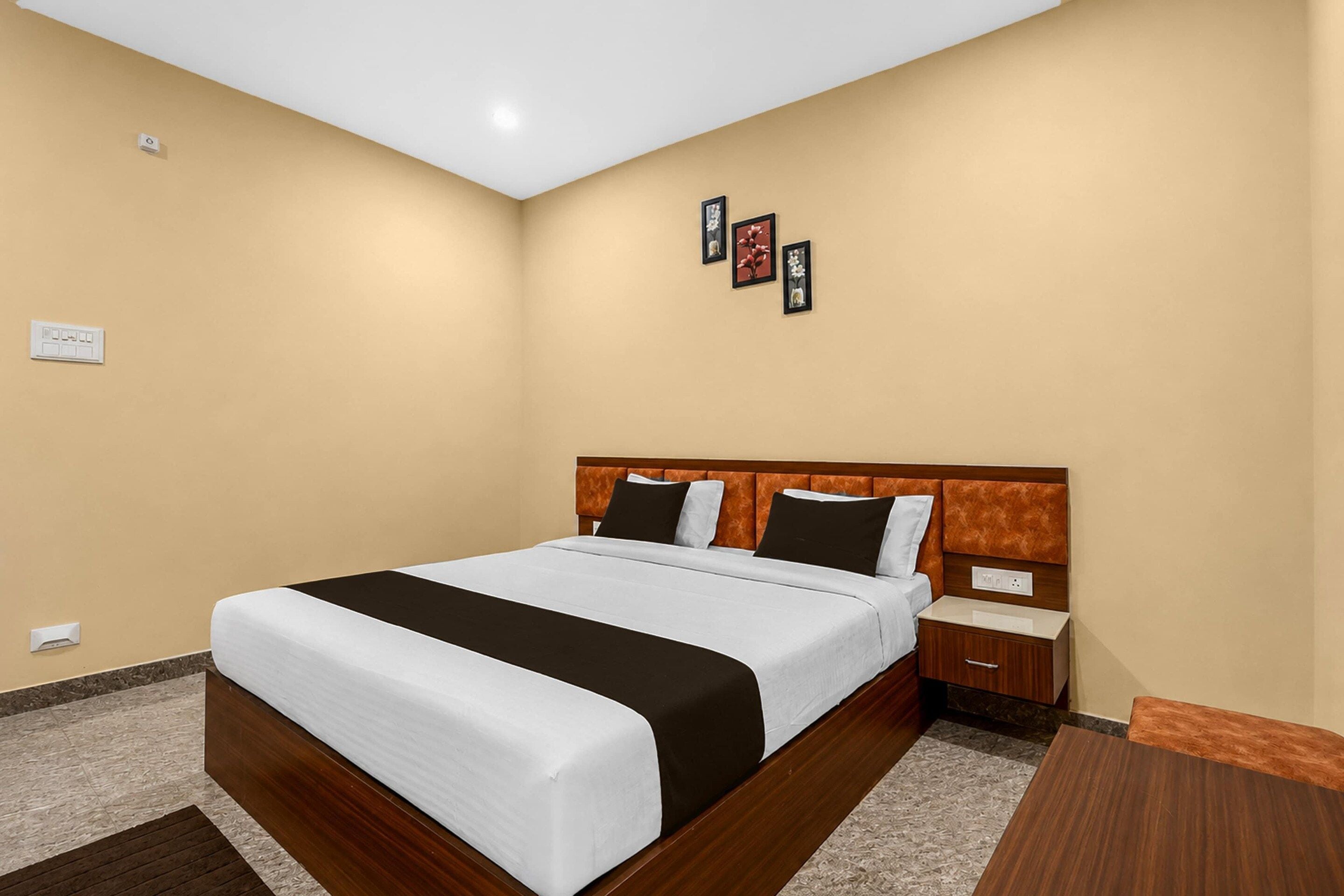 A hotel room with a bed, bedside tables, a nightstand, and a wall-mounted power outlet.