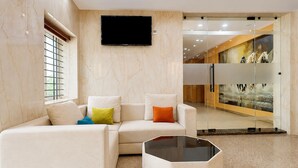 A modern hotel lobby with a sectional sofa, a glass partition, and a mounted television. - Deluxe JR Royals (Golmuri)