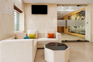 A modern hotel lobby with a sectional sofa, a glass partition, and a mounted television. - Deluxe JR Royals (Golmuri)