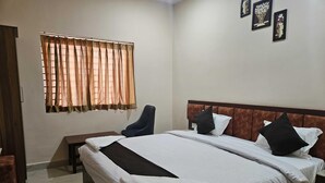Habitación de hotel con una cama grande, una silla, una mesita de noche y un ventanal con cortinas.