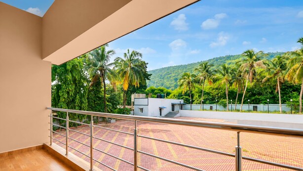 A balcony with a metal railing overlooking a paved area with palm trees and a building in the background. - Deluxe JR Royals (Golmuri)