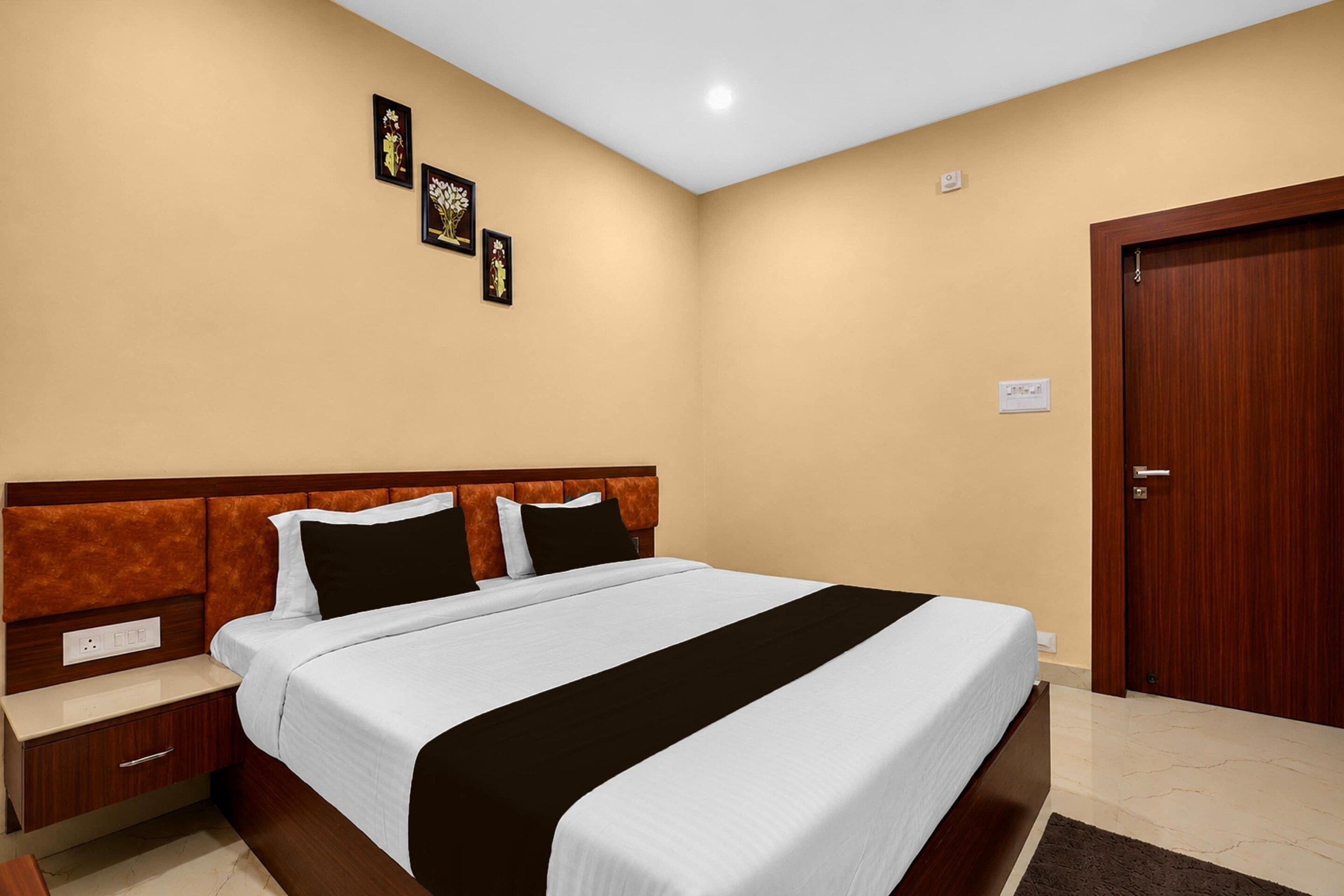 A hotel room with a bed, nightstands, a wooden door, and wall-mounted artwork.