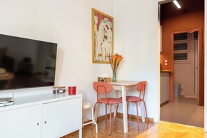 Ein Zimmer mit Fernseher, einem weißen Schrank, zwei roten Stühlen, einem Tisch und einem Bild an der Wand.